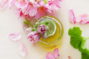 Glass bottle of golden botanical oil surrounded by delicate pink flowers.